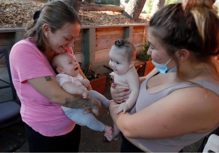 two mothers face each other holding smiling babies